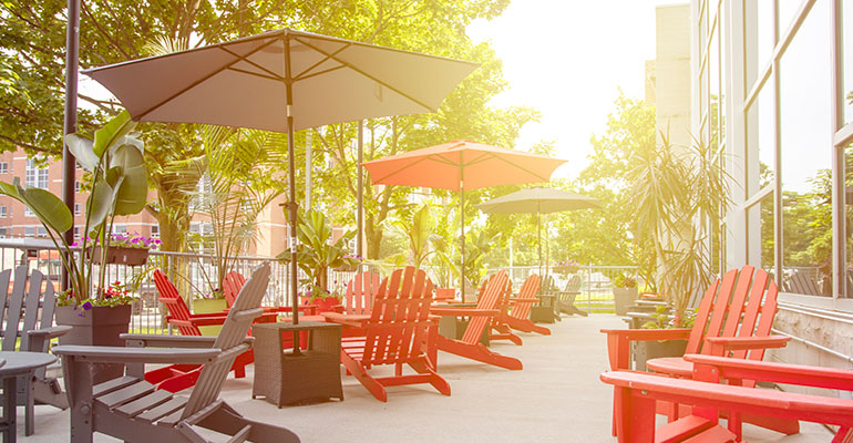 The patio of the Oasis at Fanshawe College. Red and green chairs are shown, as are tables and umbrellas.
